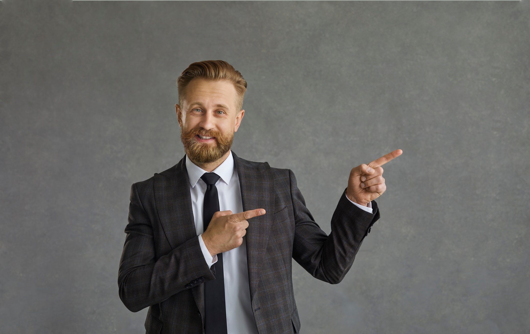 Businessman in Suit Standing against Grey Background Points Both Index Fingers Away